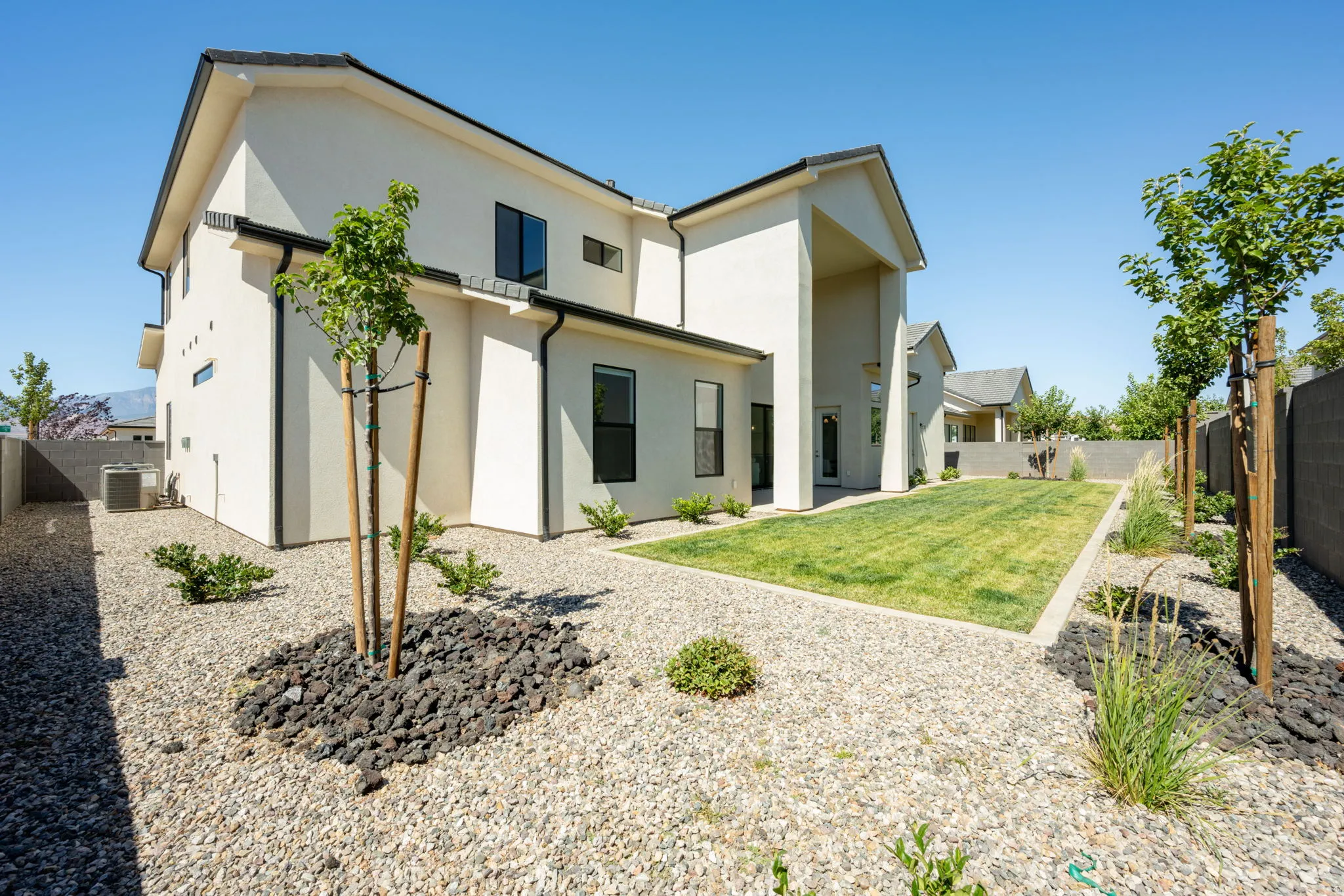 Spacious backyard featuring a manicured lawn, gravel landscaping, established young trees, and a stucco exterior with dark-framed windows