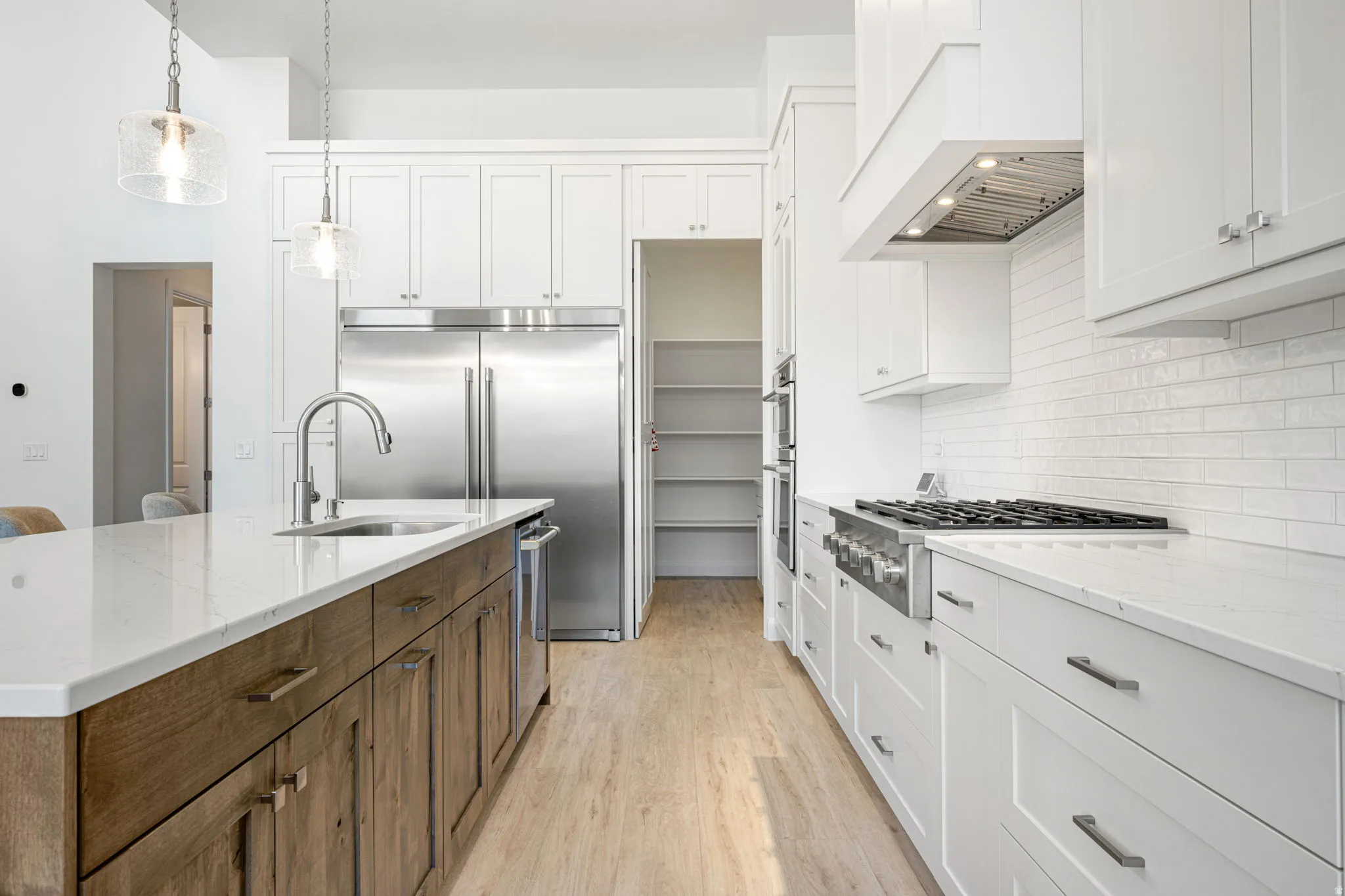Contemporary kitchen featuring white shaker cabinetry, stainless steel appliances, a center island with a wood-finish base and quartz countertop, and light wood-finish flooring