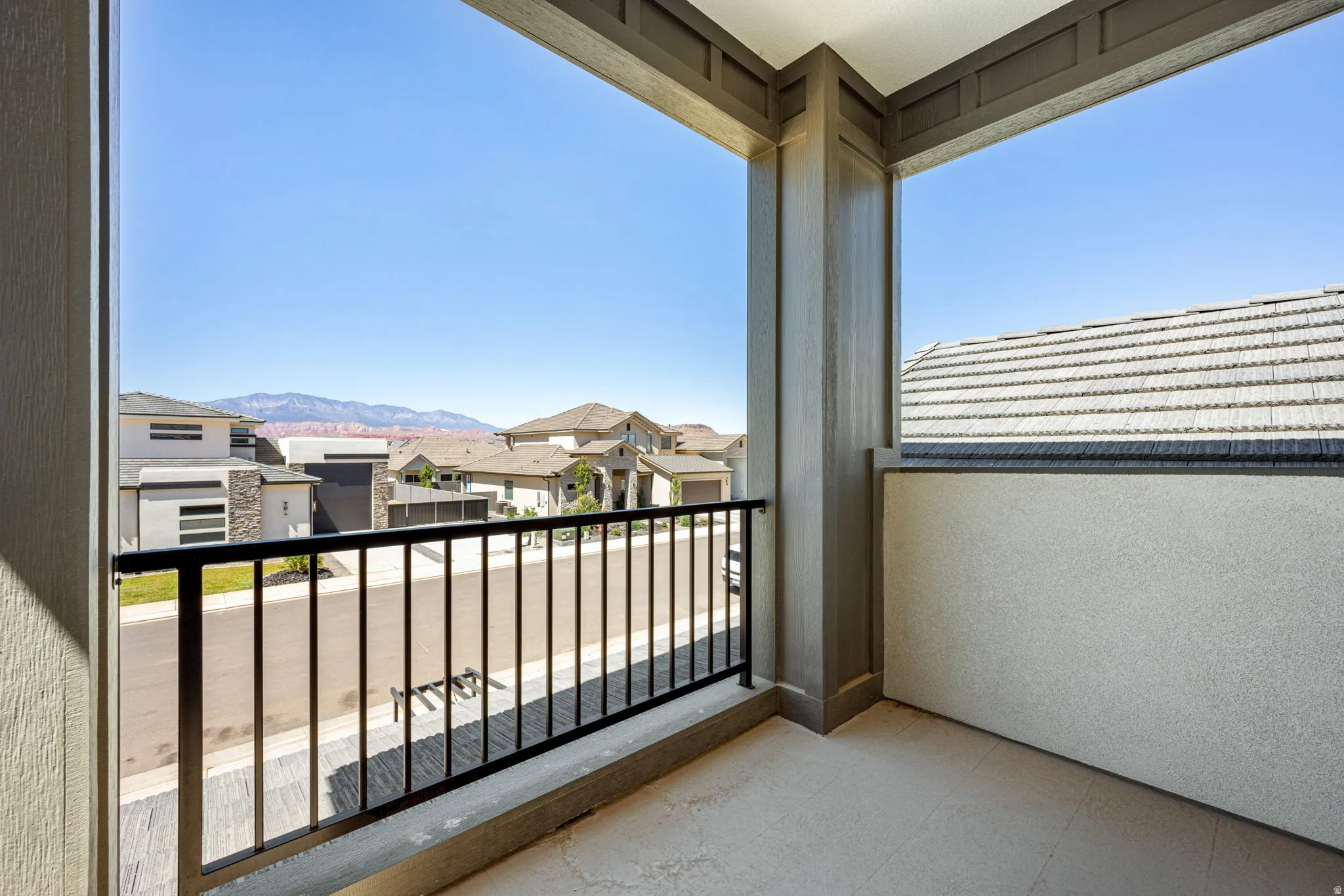 Private outdoor balcony featuring a black metal railing, textured stucco walls, and a durable concrete floor