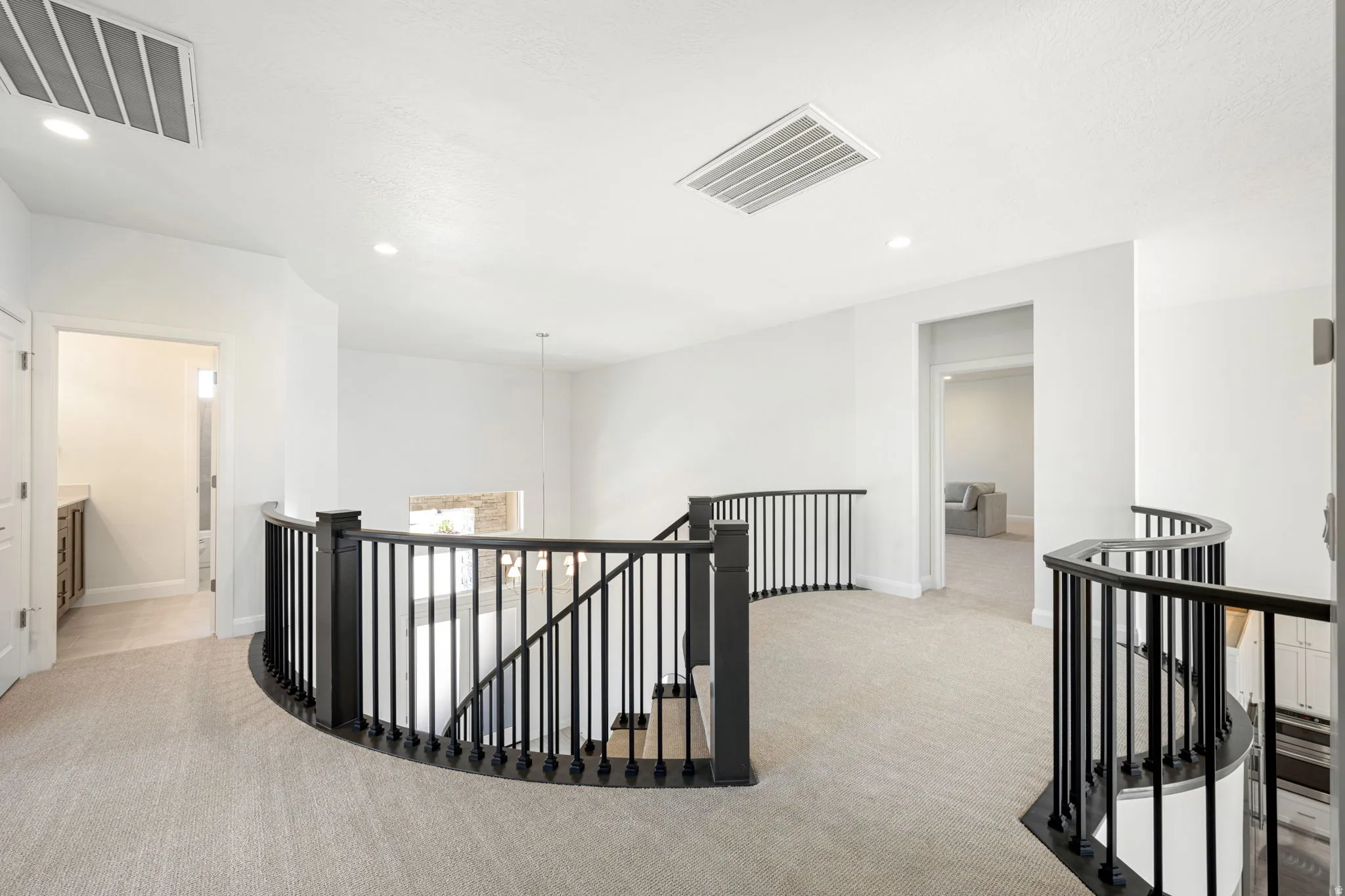 Curved landing featuring black wrought iron balusters, white walls, recessed lighting, and light-toned carpeting