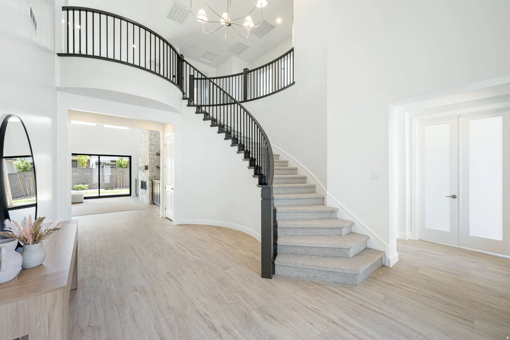 Grand foyer featuring a curved staircase with black wrought iron balusters and light gray carpeting, wood-finish flooring, and double-height ceilings