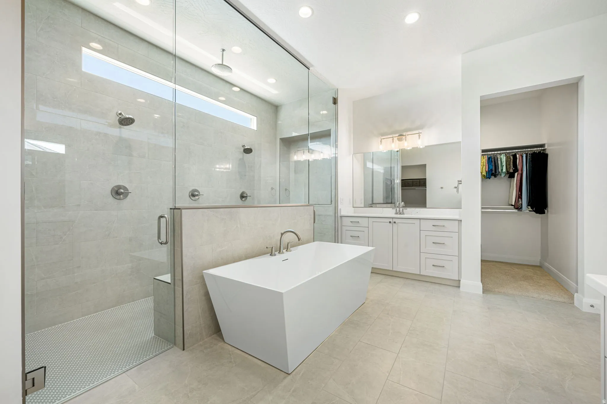 Spacious bathroom featuring a freestanding soaking tub, a large glass-enclosed shower with multiple showerheads, and light-toned tile flooring