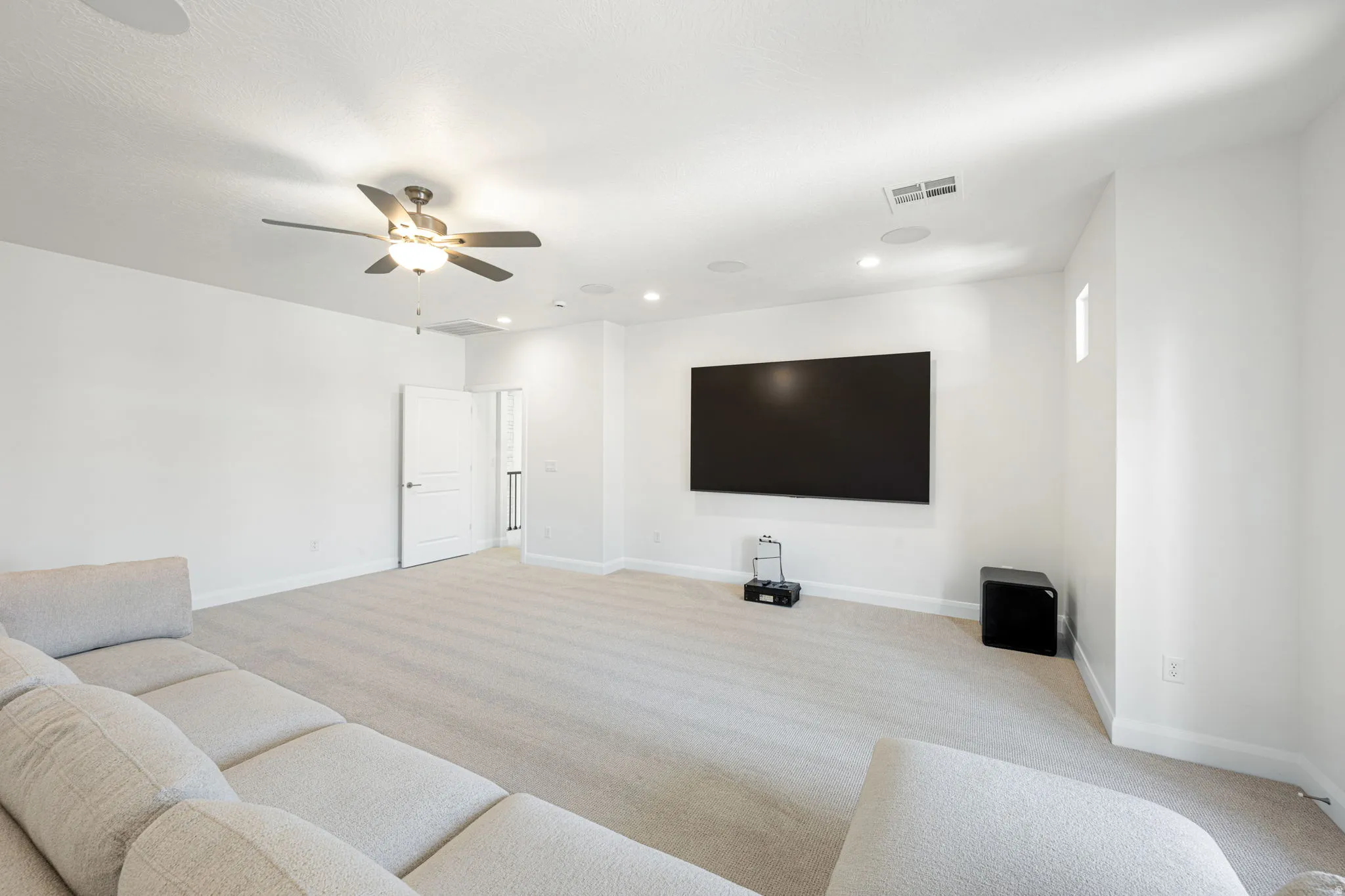 Expansive room featuring a large wall-mounted screen, recessed lighting, and a ceiling fan