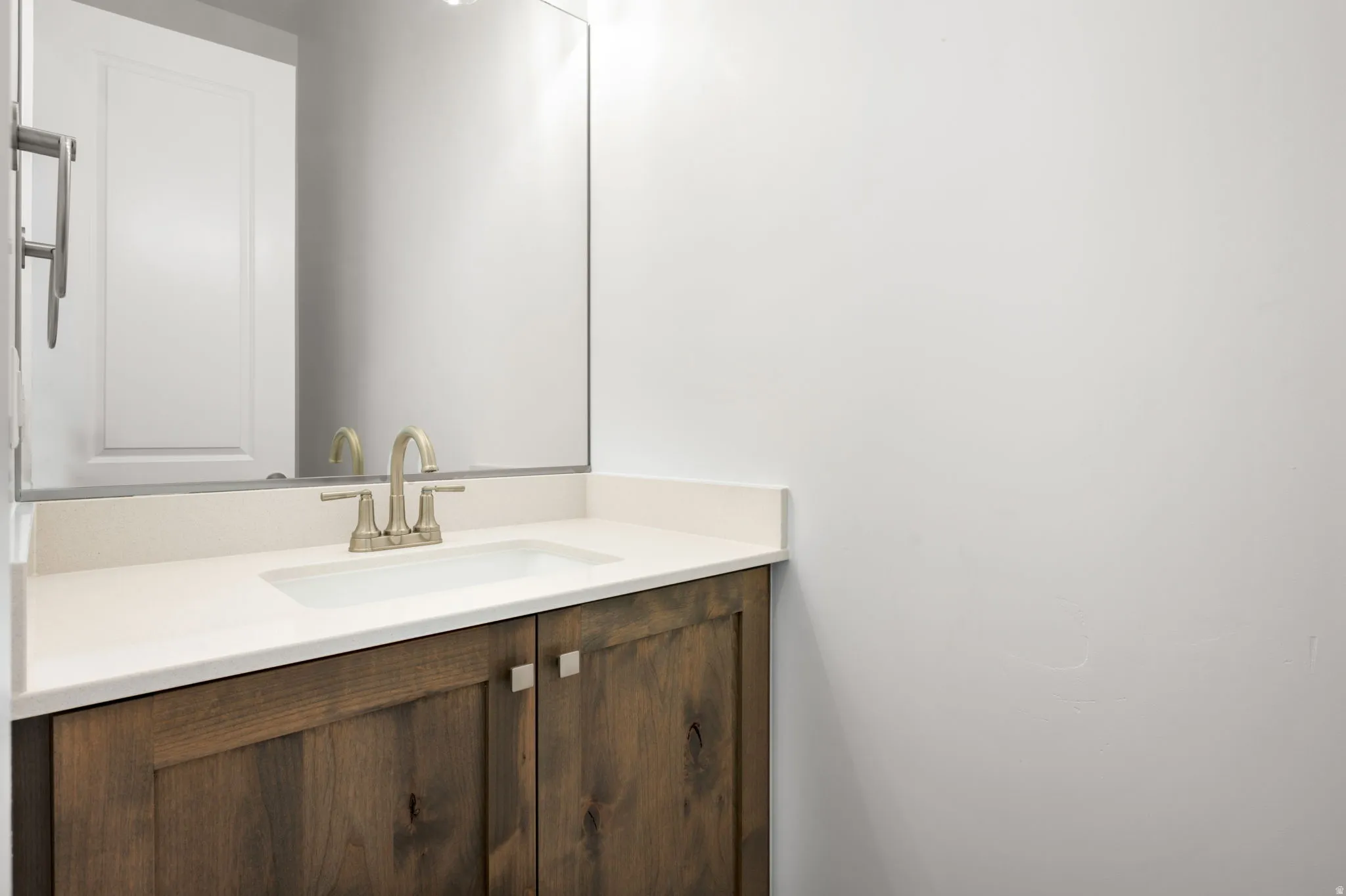 Bathroom vanity featuring wood-finish cabinetry with contemporary square pulls, an integrated rectangular sink, and a light-toned countertop