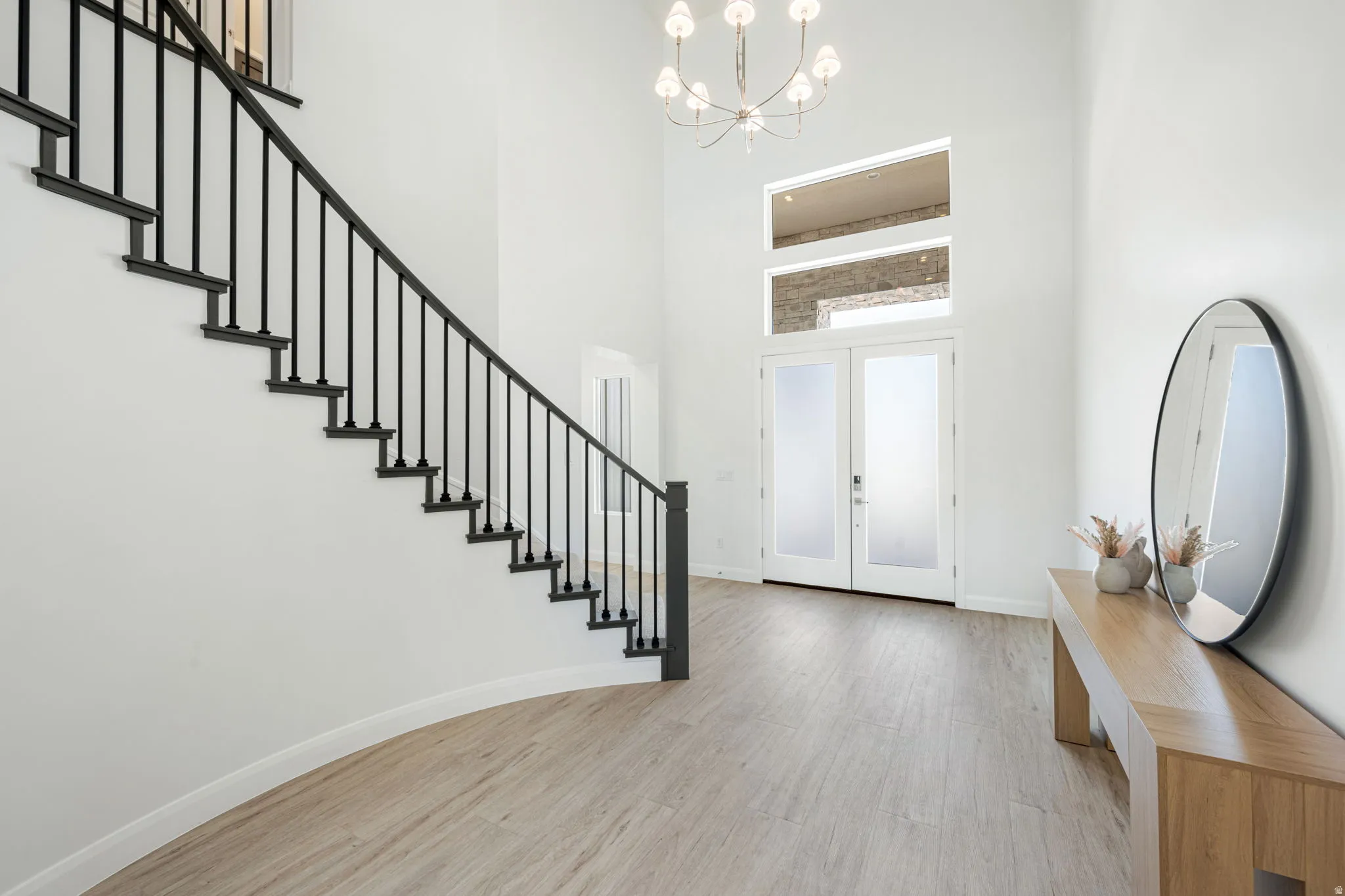 Grand foyer featuring a curved staircase with black wrought iron balusters, double entry doors with frosted glass panels, transom windows, a high ceiling, and wood-finish flooring