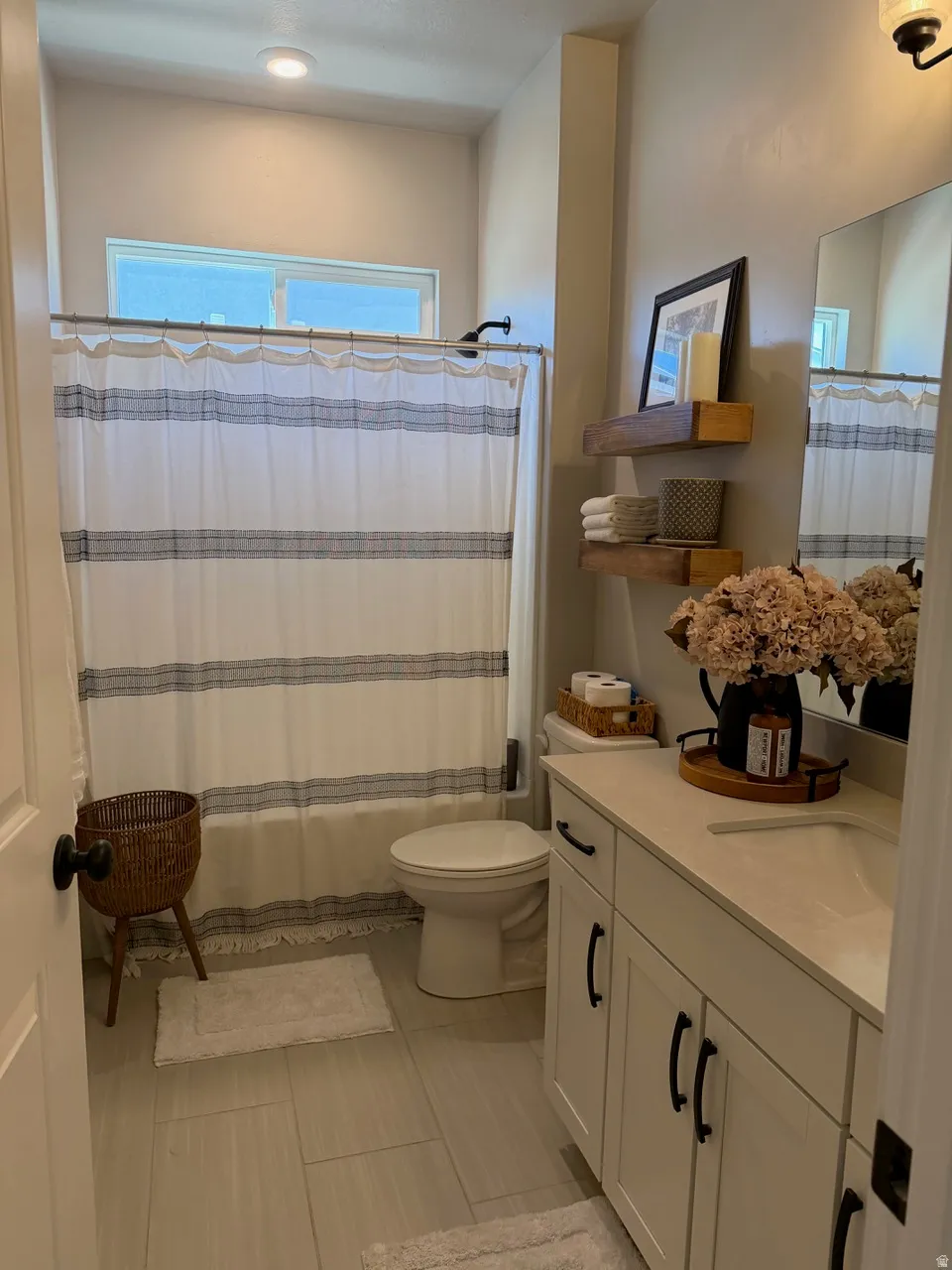 Bathroom featuring a shower-tub combination with a window, single vanity with shaker-style cabinetry, dark hardware, light countertop, and tile flooring