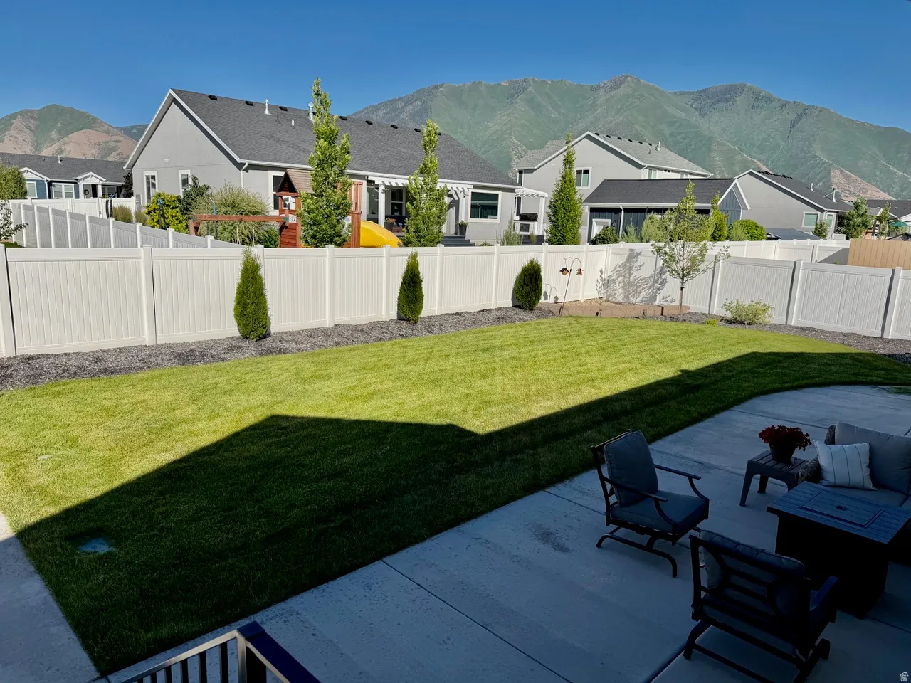 Expansive backyard featuring a spacious concrete patio, manicured lawn, full vinyl fencing, and distant mountain scenery