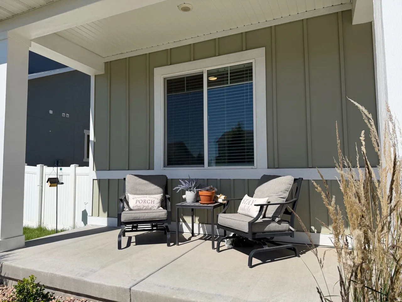 Covered front porch featuring a concrete surface, vertical plank siding, a white vinyl fence, and a modern window