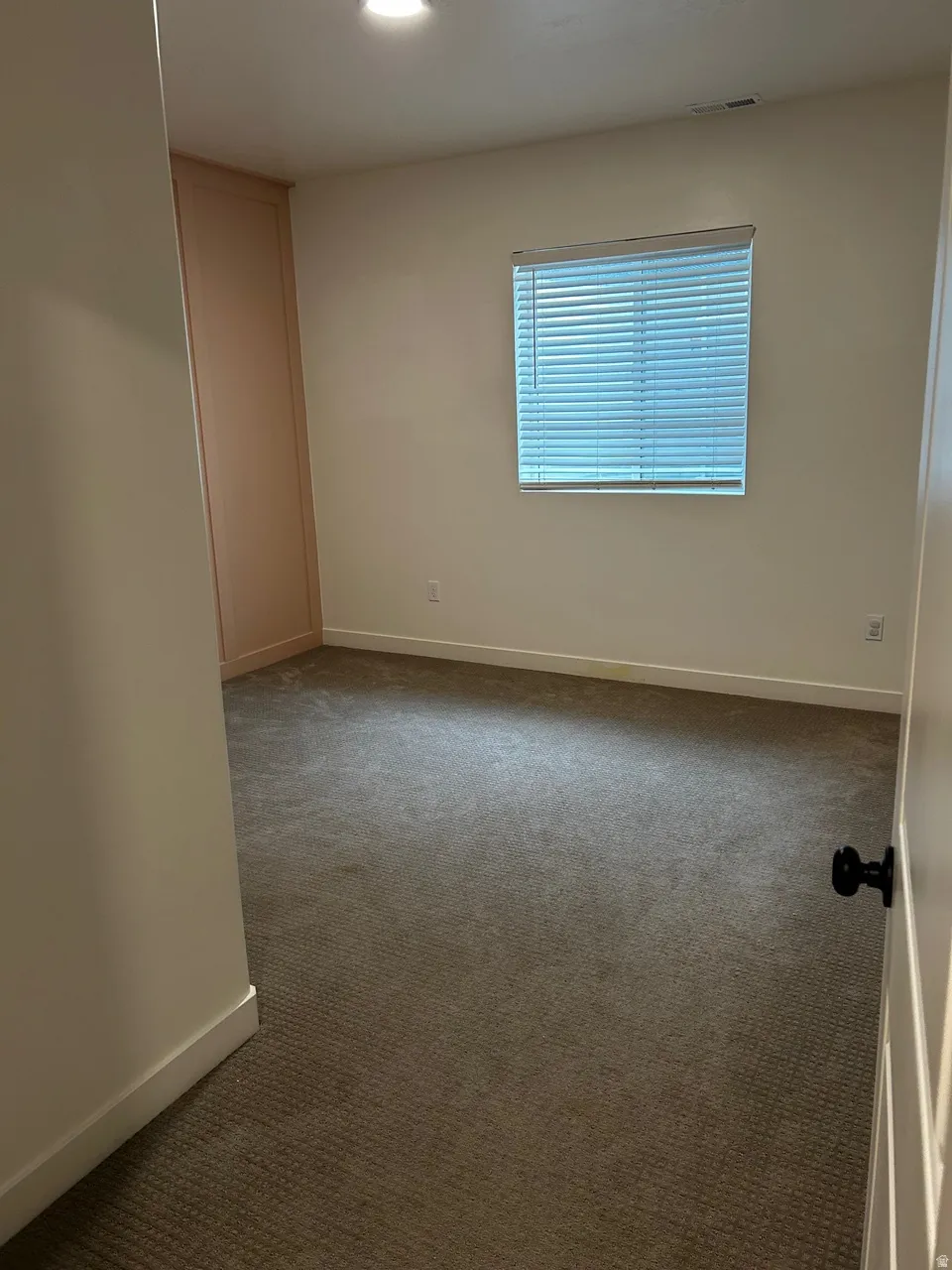 Carpeted room featuring a window with blinds, recessed lighting, and a built-in vertical cabinet