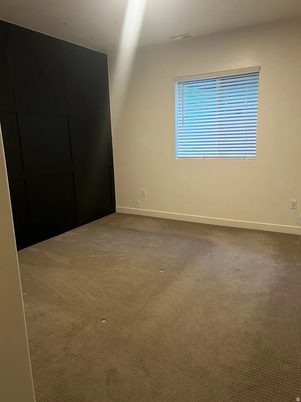 Room featuring a black accent wall with panel detailing, light-toned wall paint, a window with horizontal blinds, and carpeted flooring
