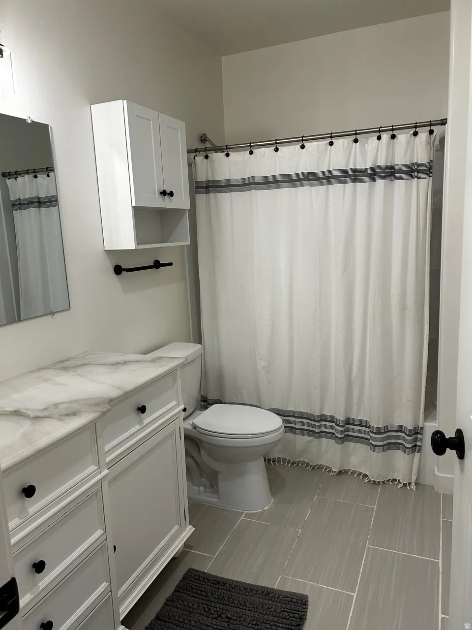 Bathroom featuring a white vanity with a stone-finish countertop, coordinating overhead cabinetry, a white toilet, and large format floor tiling