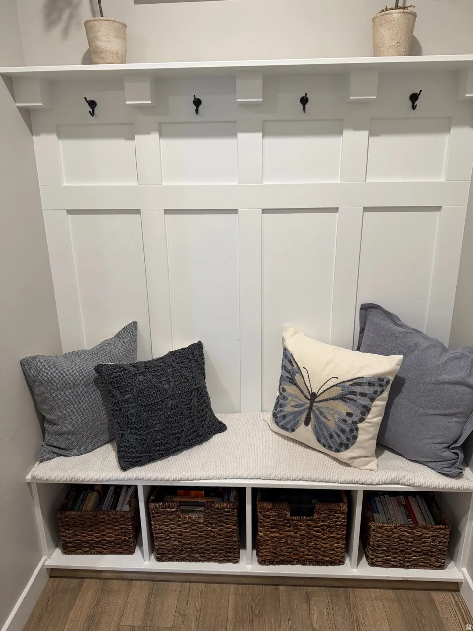Built-in mudroom bench featuring white paneling, multiple coat hooks, an upper shelf, and integrated lower storage cubbies