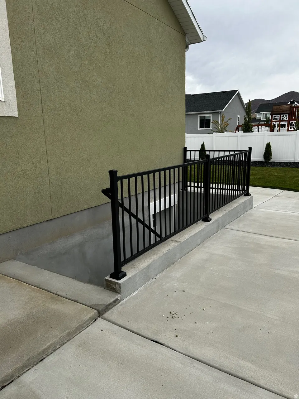 Exterior featuring a stucco finish, black metal railing, concrete patio, and white vinyl fencing
