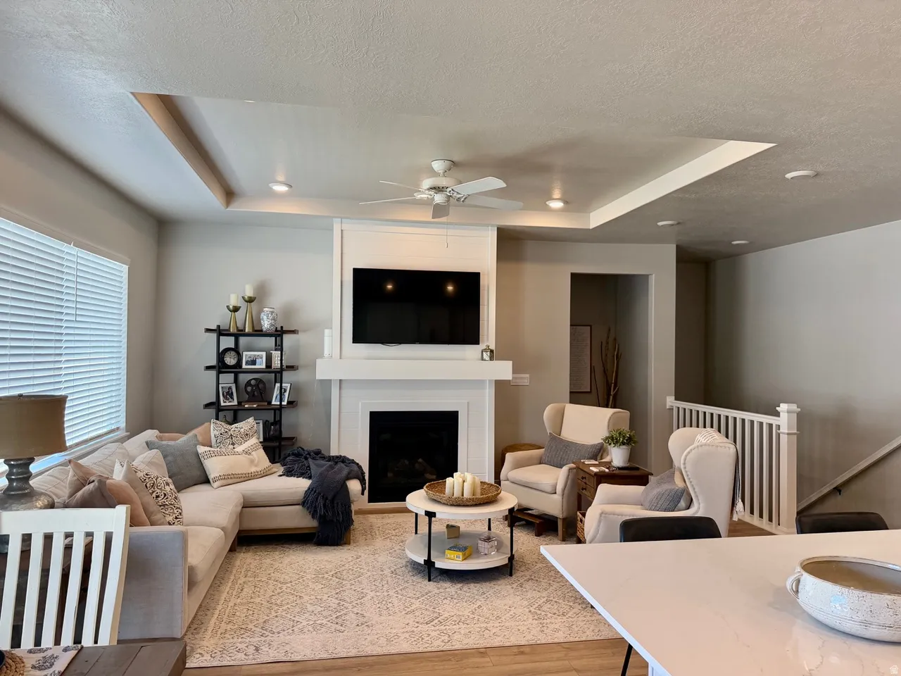 Living area featuring a fireplace with a white mantel, recessed lighting, ceiling fan, wood-finish flooring, and a tray ceiling