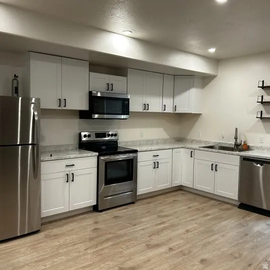 Kitchen featuring white shaker-style cabinetry, stainless steel appliances, light-toned countertops, wood-finish flooring, and recessed lighting
