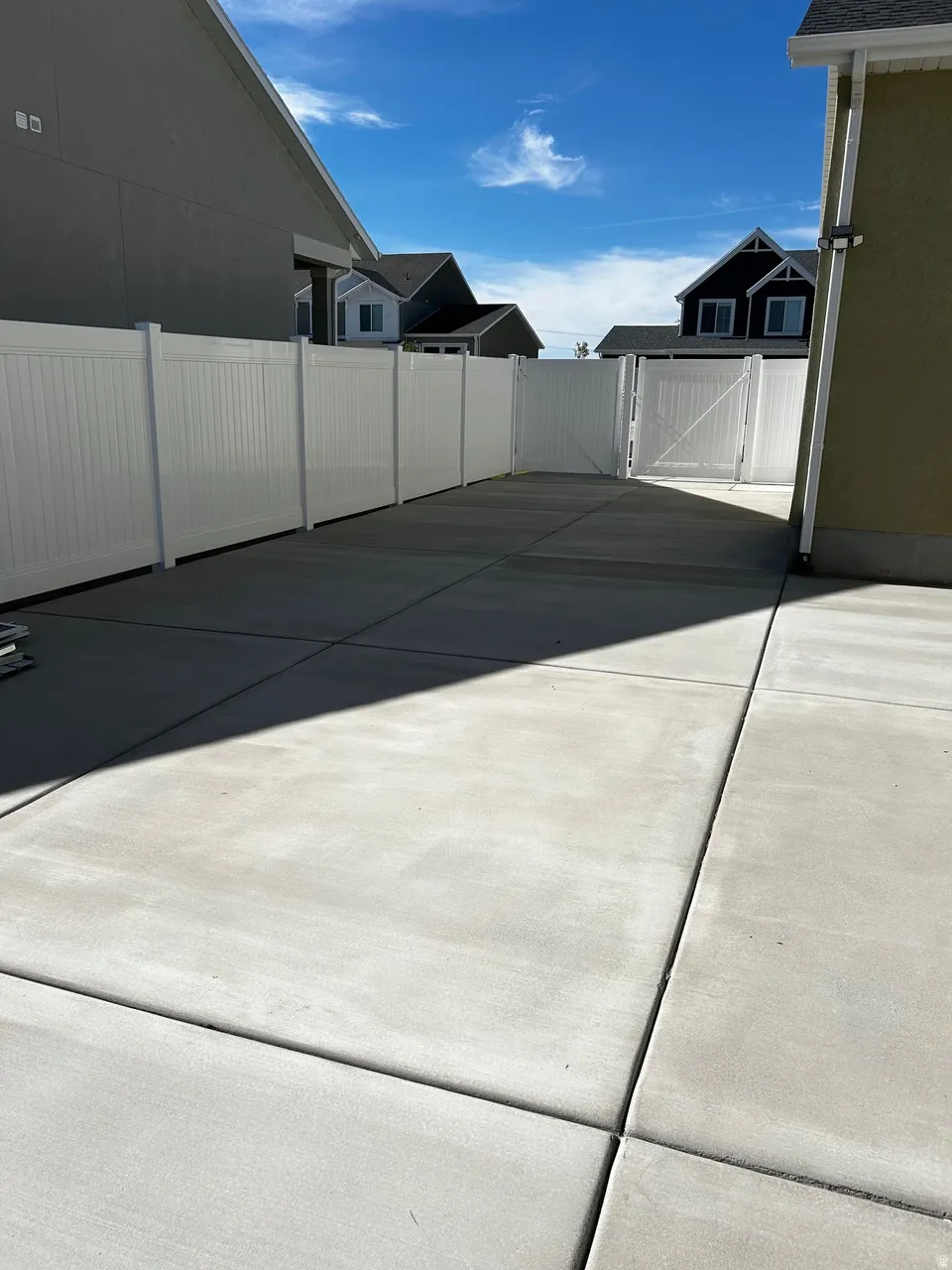 Expansive concrete driveway framed by a tall white privacy fence with a matching privacy gate