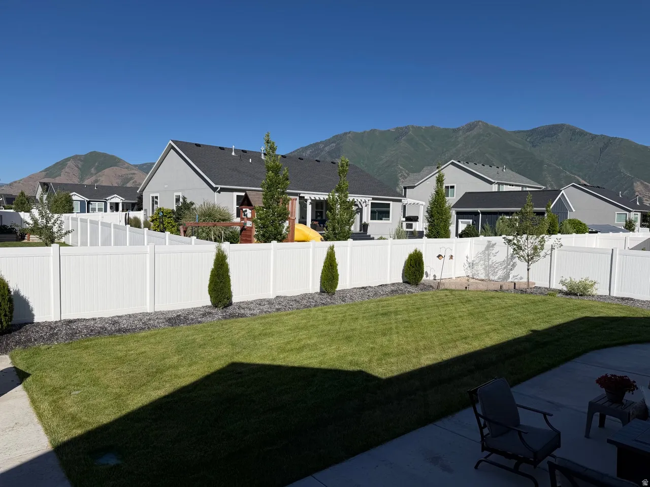 Expansive backyard with a manicured lawn, established landscaping, and a surrounding white privacy fence