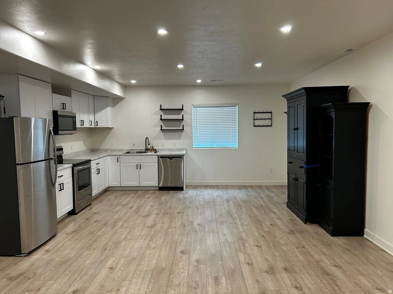 Open-concept living space featuring a full kitchen with stainless steel appliances, white cabinetry, and light-toned countertops