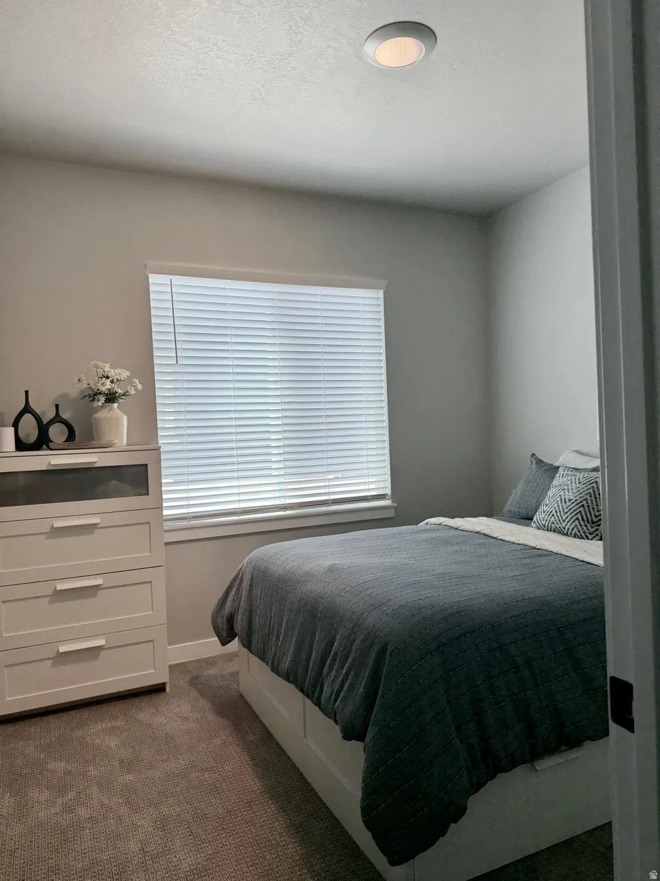Neutral wall color, recessed ceiling lighting, textured carpet flooring, window with horizontal blinds, and baseboard trim