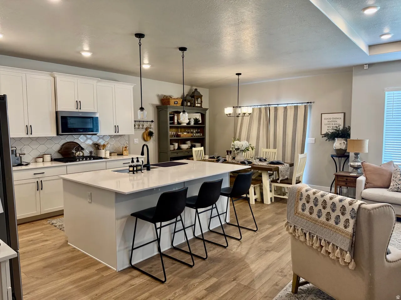Open-concept kitchen featuring an island with integrated sink, white cabinetry with dark hardware, a tile backsplash, and stainless steel appliances
