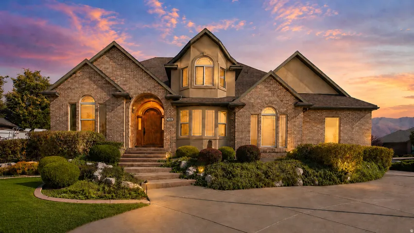 Stone and stucco exterior featuring a prominent arched entry, multiple arched windows, mature landscaping, concrete driveway, and concrete front steps