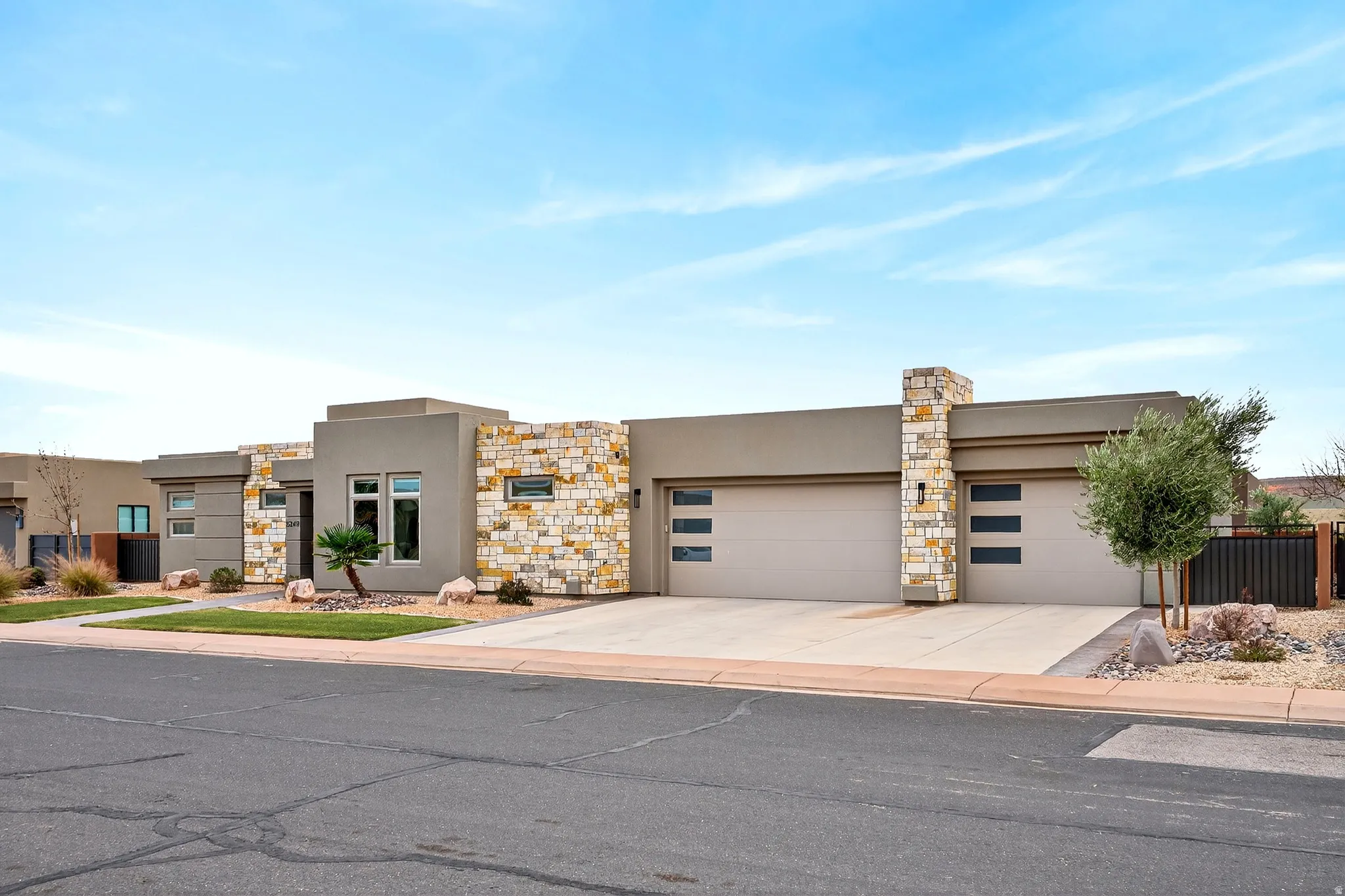 Modern single-story stucco residence with stone veneer accents, dual garage doors with frosted glass panels, an integrated exterior light fixture, and a concrete driveway
