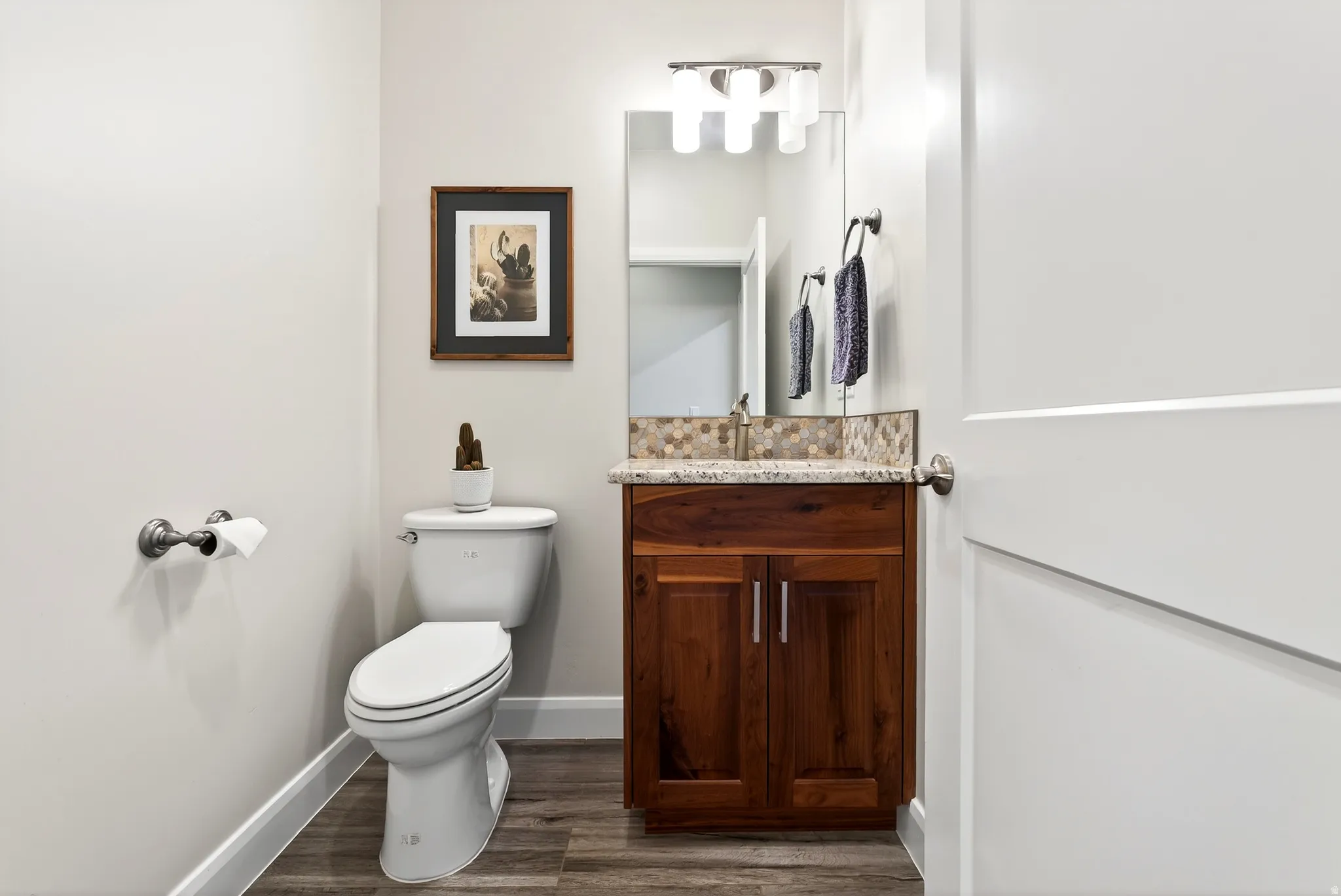 Bathroom featuring a white toilet, wood-finish vanity with granite countertop, and mosaic tile backsplash