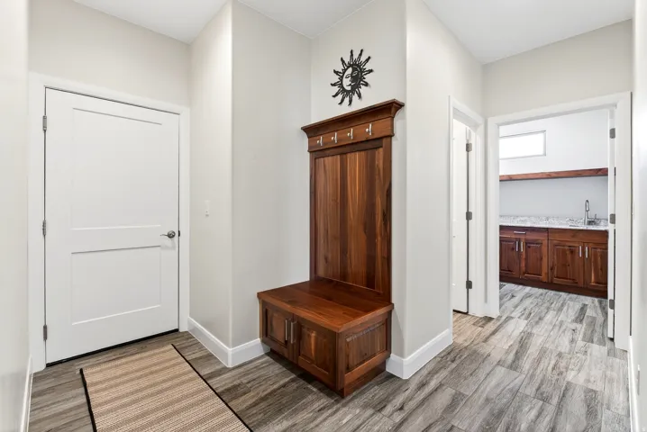 Entryway featuring wood-finish flooring, a built-in wooden coat rack with bench seating and storage, and a white two-panel door