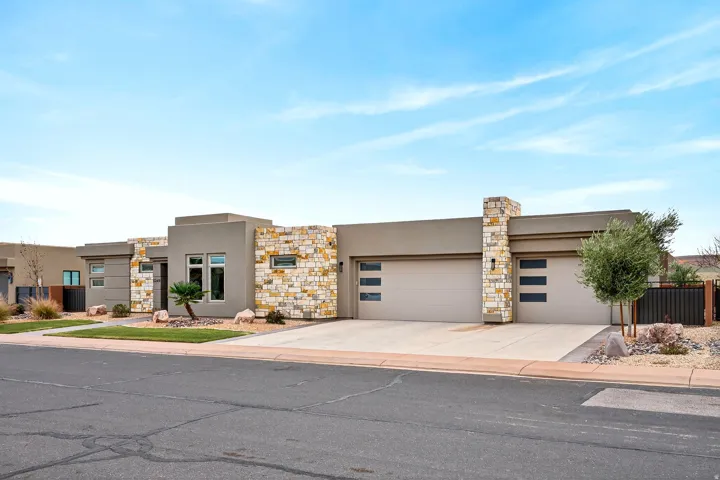 Modern single-story stucco residence with stone veneer accents, dual garage doors with frosted glass panels, an integrated exterior light fixture, and a concrete driveway