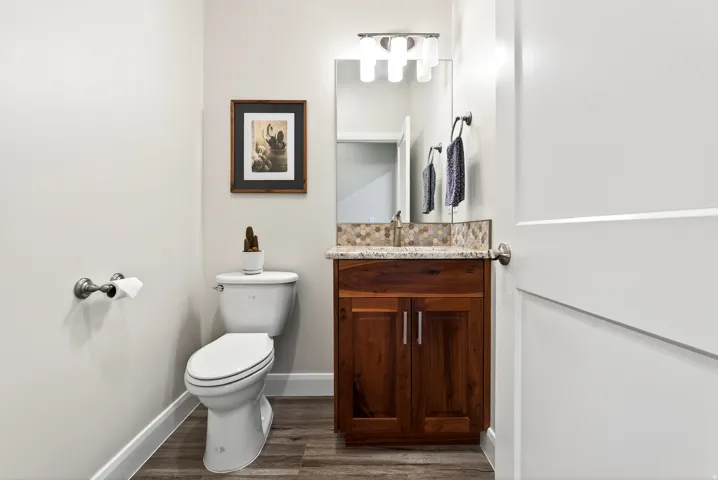 Bathroom featuring a white toilet, wood-finish vanity with granite countertop, and mosaic tile backsplash