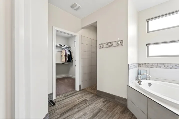 Bathroom featuring an integrated soaking tub with mosaic tile surround, walk-in shower with pebble flooring, wood-finish flooring, and two horizontal windows