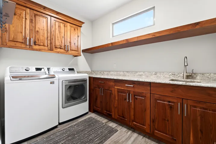 Dedicated laundry space featuring wood-finish cabinetry, a built-in sink with a gooseneck faucet, light-toned countertop, and wood-finish flooring
