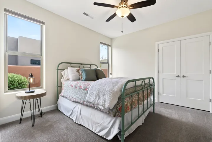 Carpeted room featuring a ceiling fan with light fixture, dual pane windows, and bi-fold doors with paneling