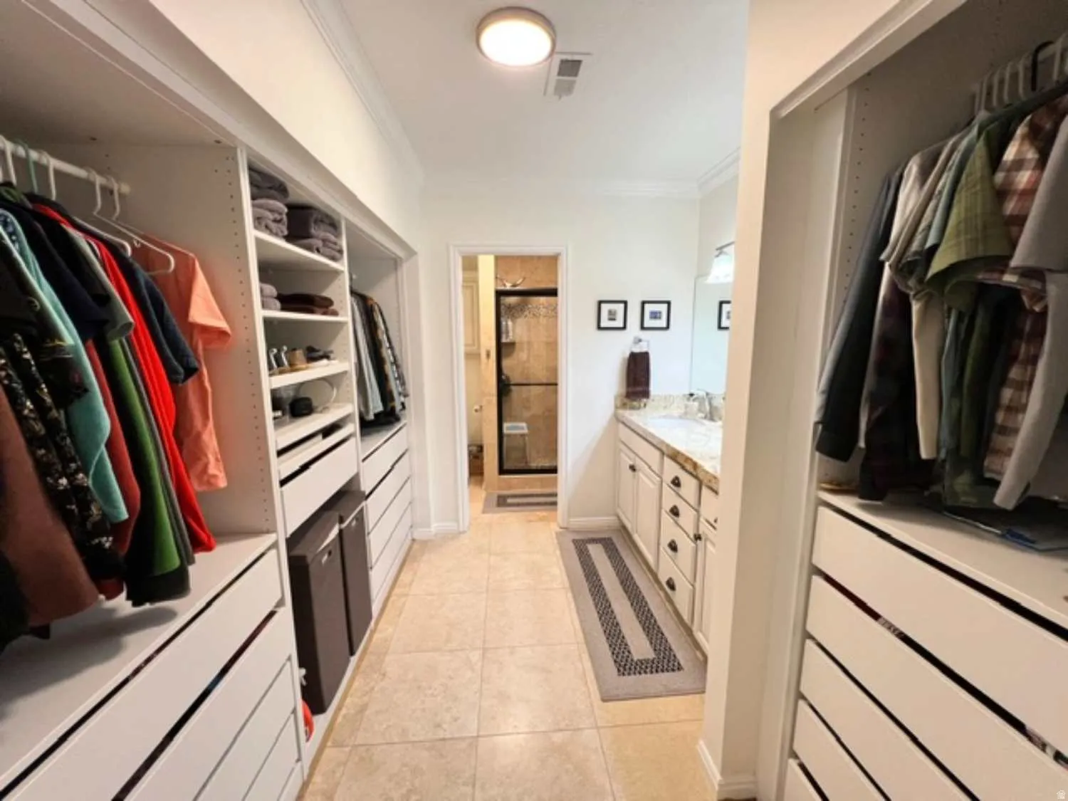 Walk-through closet featuring built-in shelving, hanging rods, drawer storage, and tile flooring