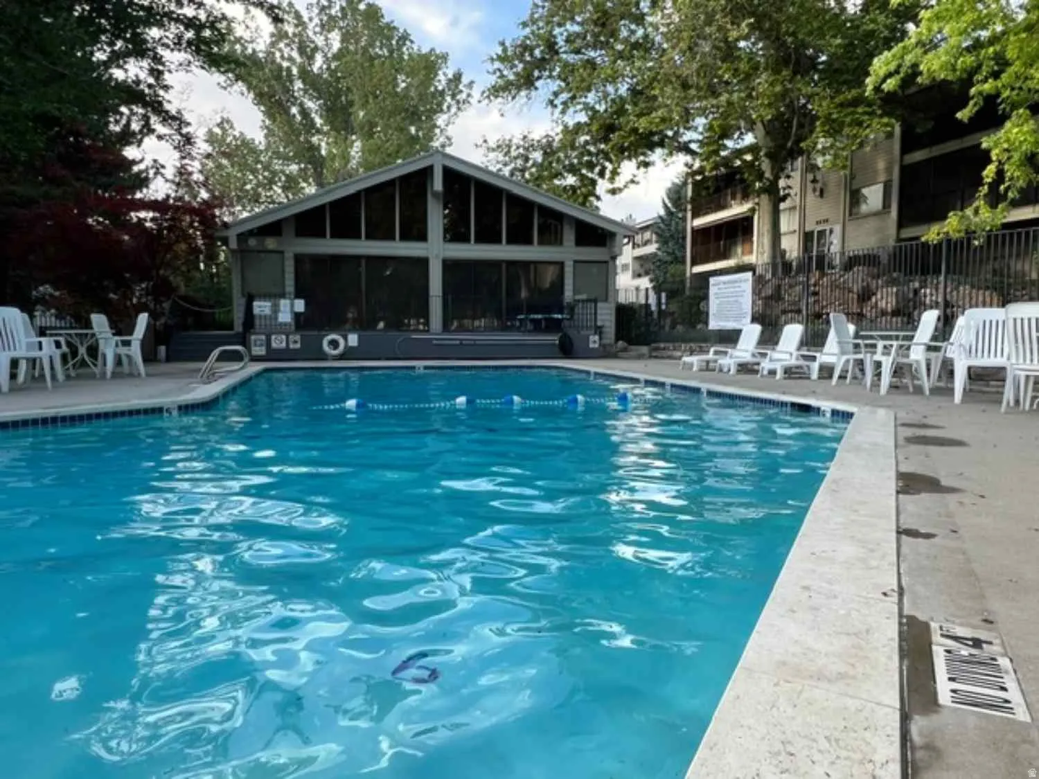 Outdoor swimming pool with a concrete surround, featuring a pool house with large windows and a sloped roof