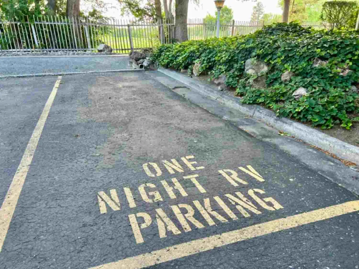 Paved parking area featuring a designated parking space, concrete curbing, and a landscaped retaining wall with abundant greenery