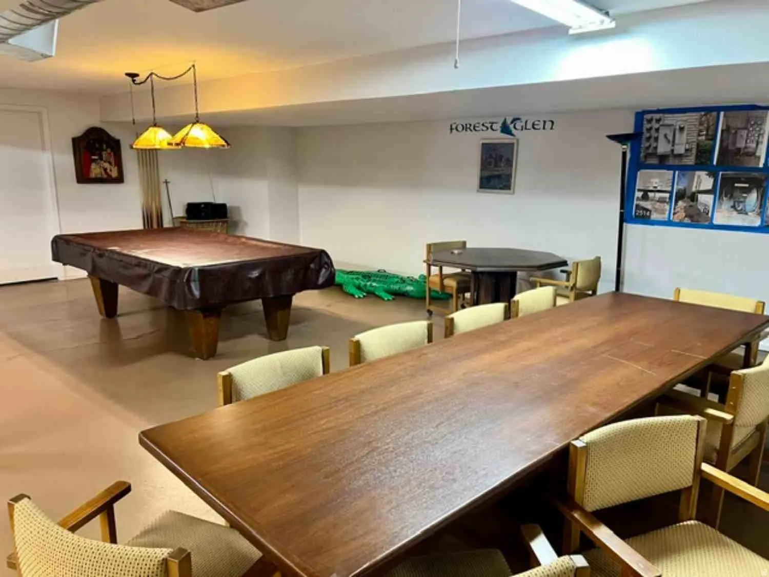 Large recreational space featuring a pool table with overhead pendant lighting, a long wood-finish table with upholstered chairs, and a smaller wood-finish table with additional seating