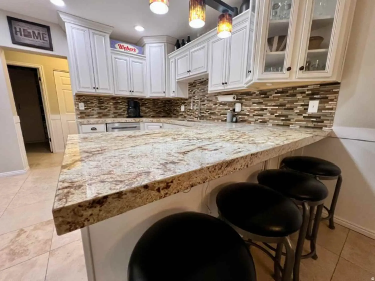 Kitchen featuring a spacious peninsula with a light-toned, variegated countertop, white cabinetry with crown molding, a multi-tone mosaic tile backsplash, and recessed lighting
