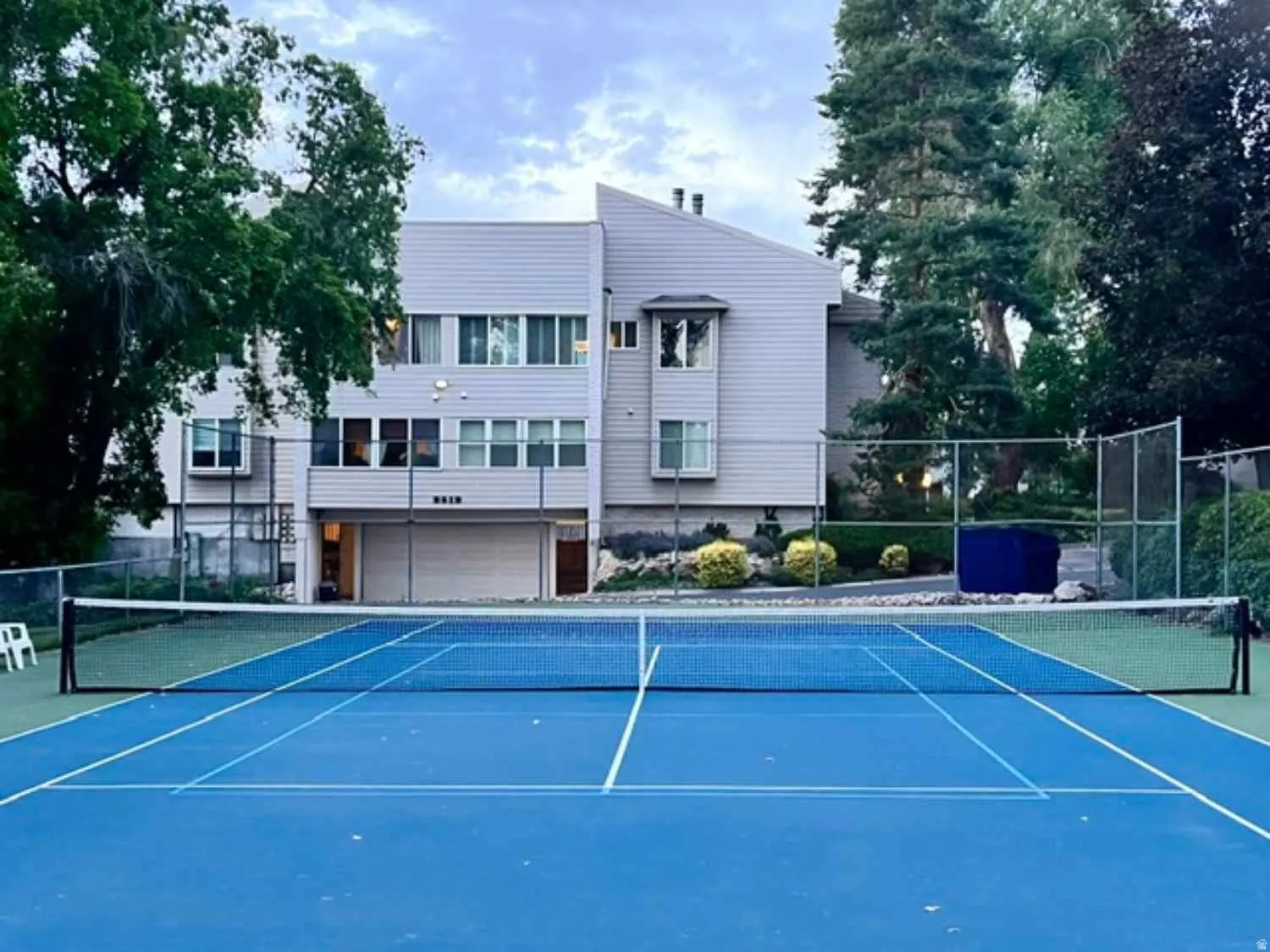 Full-size tennis court featuring a blue playing surface with white lines and a black net