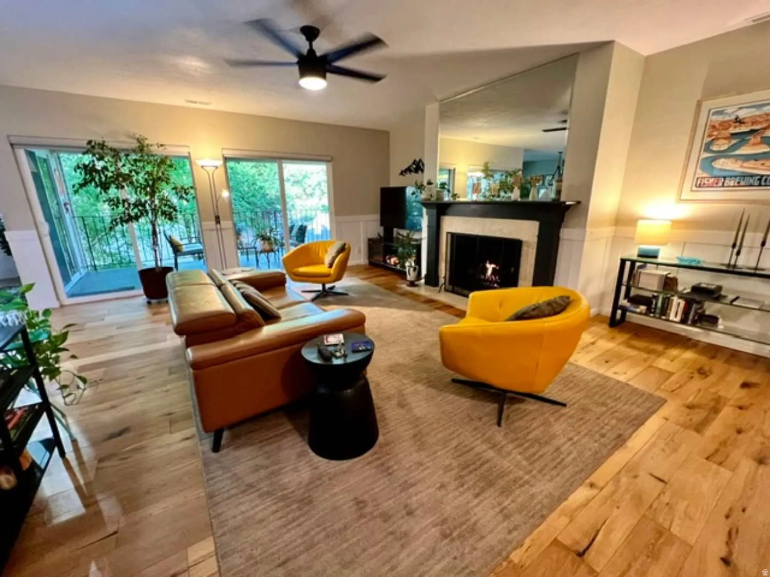 Living space featuring wood-finish flooring, a fireplace with a black mantel, an overhead ceiling fan, and sliding glass doors opening to an outdoor balcony