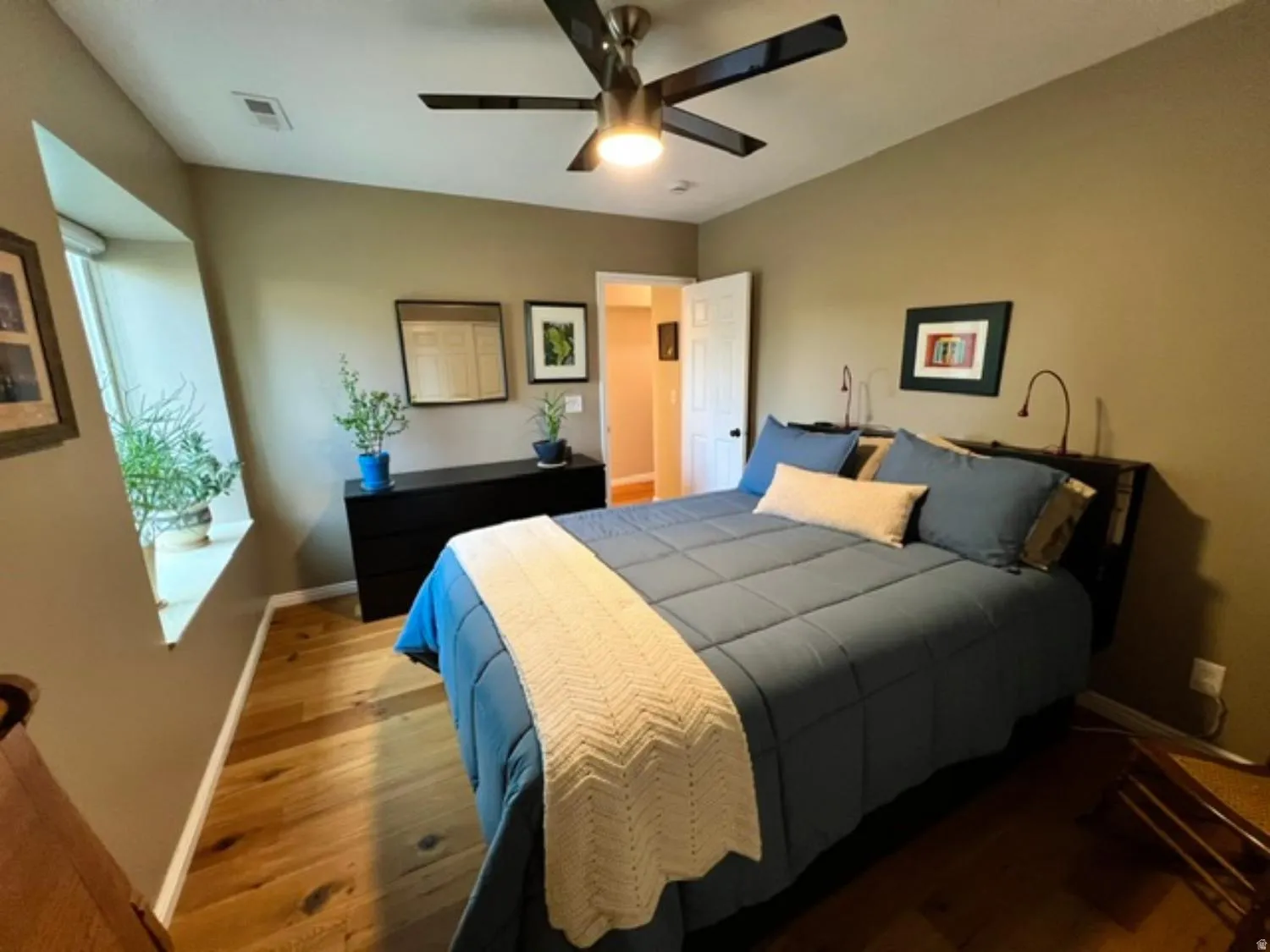 Bedroom featuring wood-finish flooring, a contemporary ceiling fan with integrated lighting, and a unique angled window design