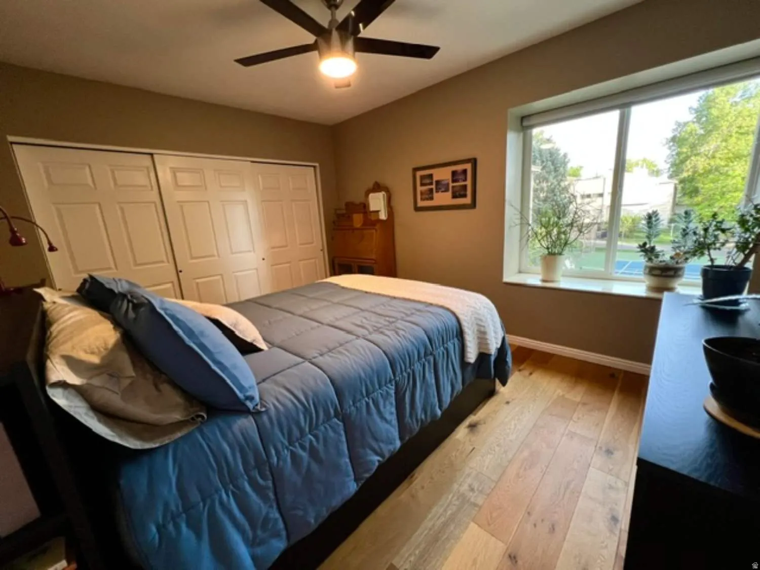 Room featuring wide-plank wood-finish flooring, a large window, a ceiling fan with integrated lighting, and multiple bi-fold closet doors