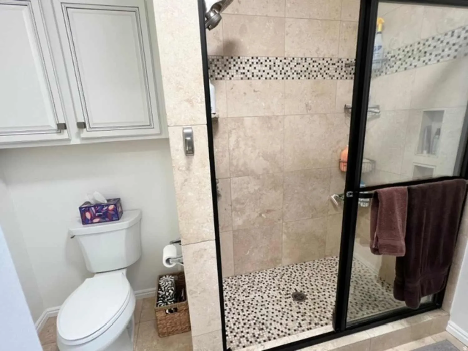 Glass-enclosed shower with a mosaic tile floor and a decorative mosaic accent strip