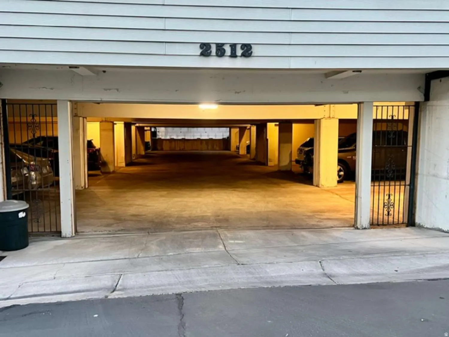 Covered parking structure featuring concrete flooring, structural support columns, and wrought iron security gates