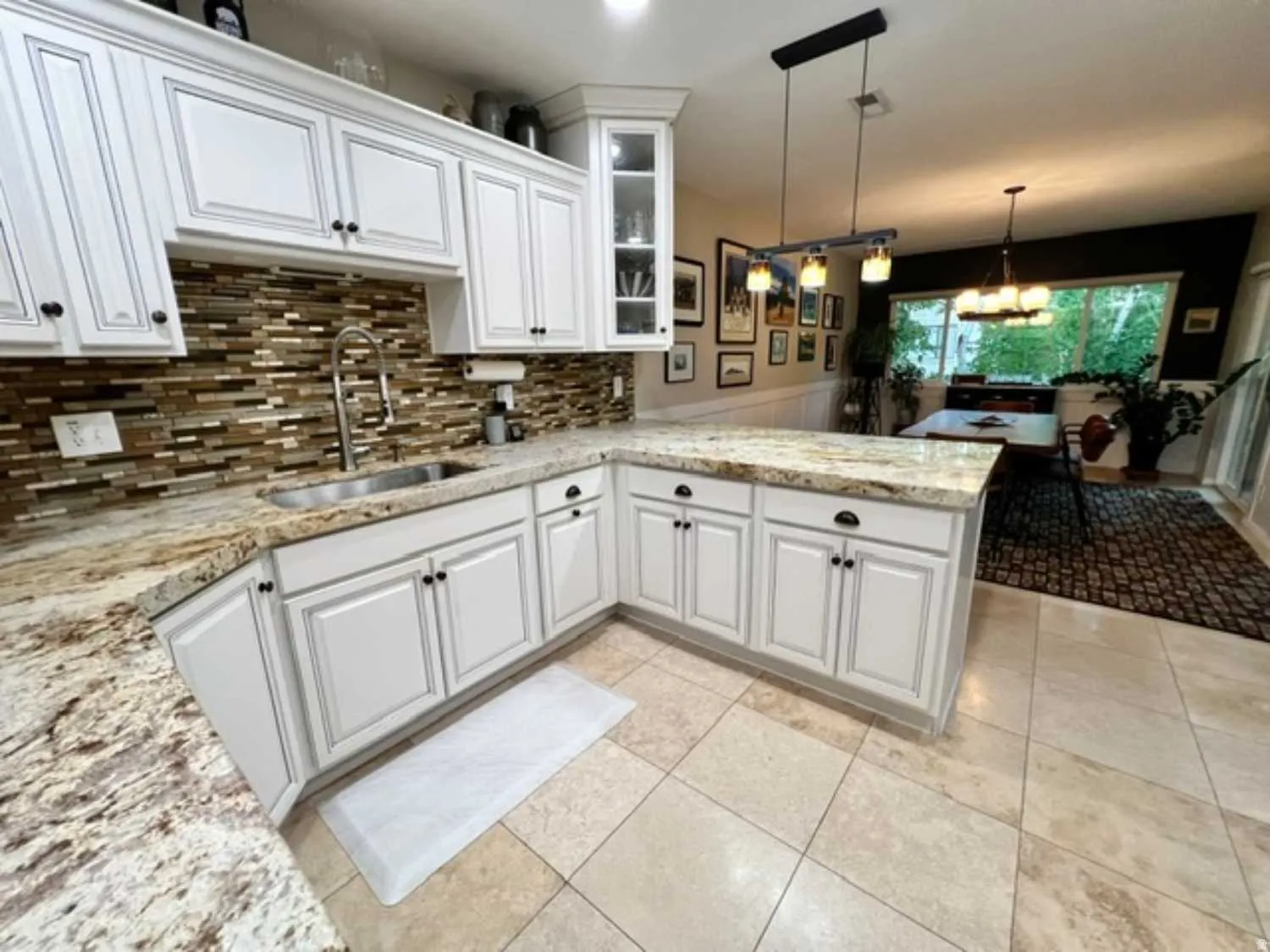 L-shaped kitchen featuring white cabinetry, light-toned stone countertops, and a full tile backsplash