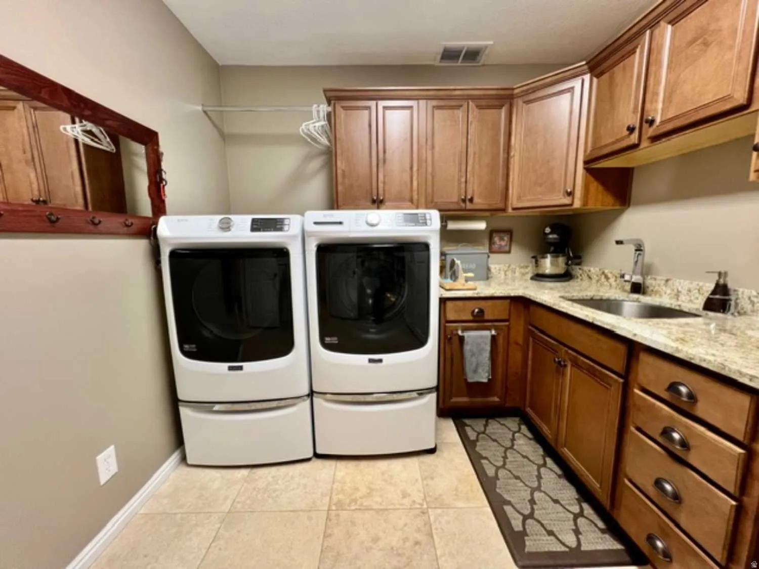Utility room with light wood cabinetry, stone-finish countertops, and a built-in stainless steel sink