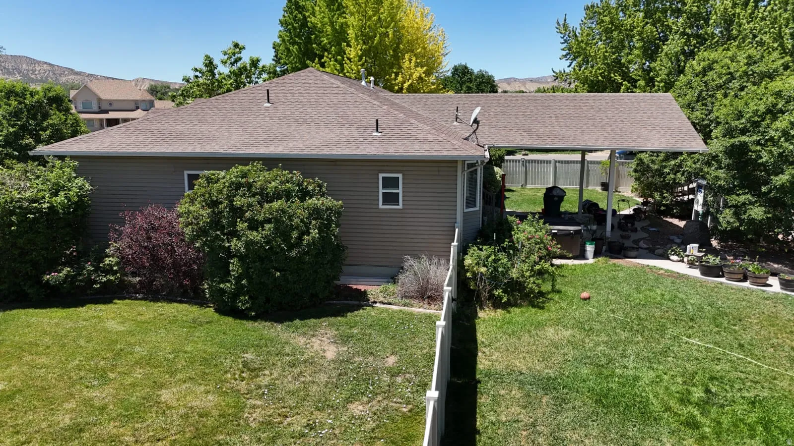 Expansive backyard featuring a manicured lawn, established landscaping, and a covered patio area
