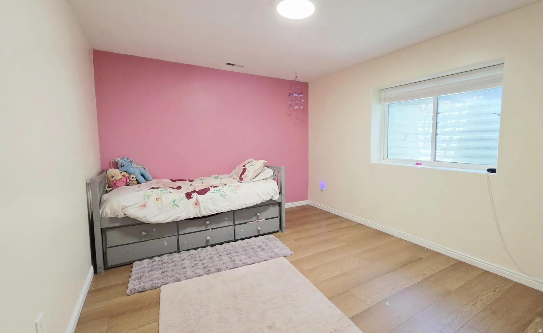 Room featuring wood-finish flooring, a pastel accent wall, and a single window with blinds