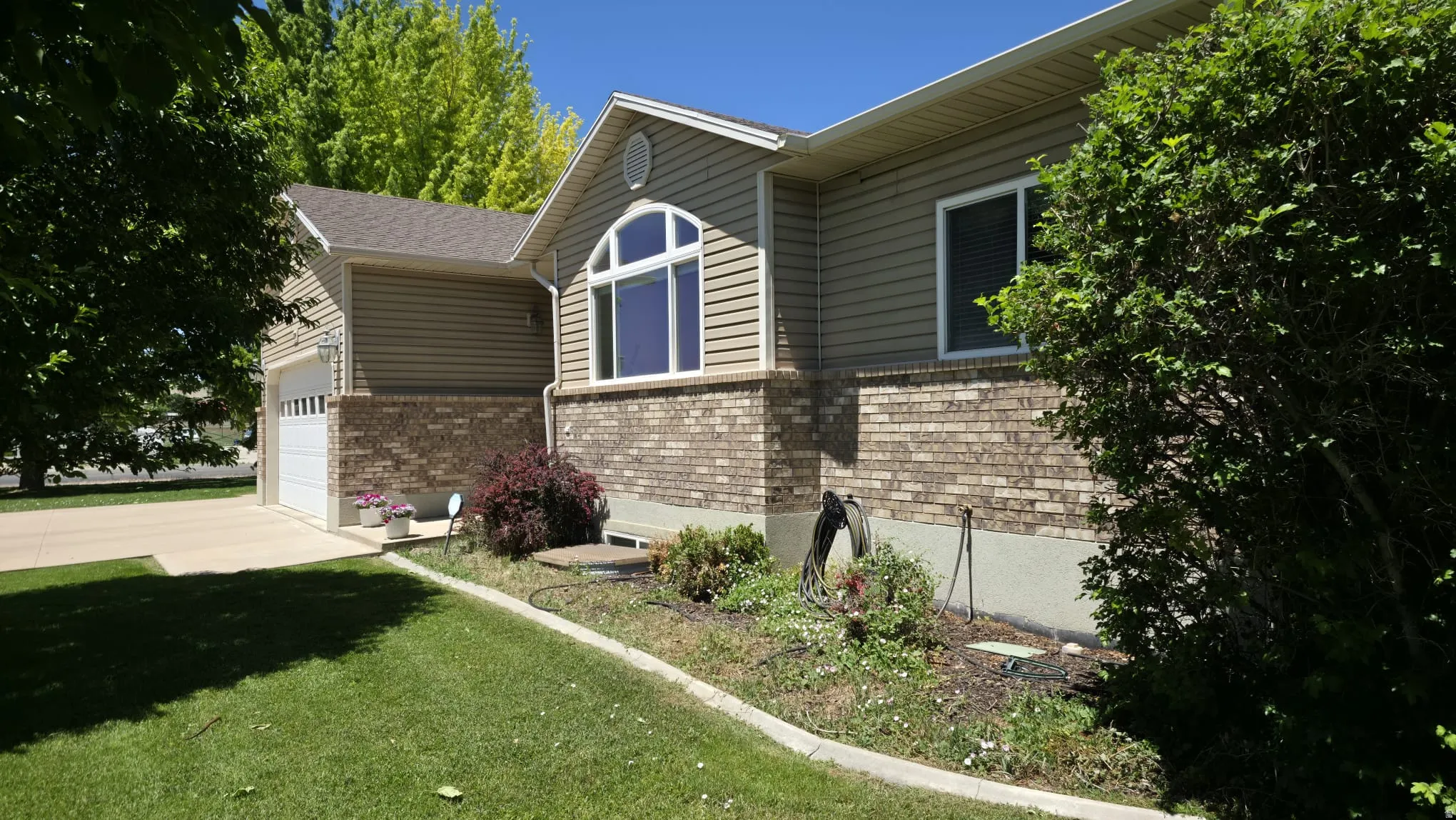 Exterior featuring tan siding, a brown brick facade, and an arched window