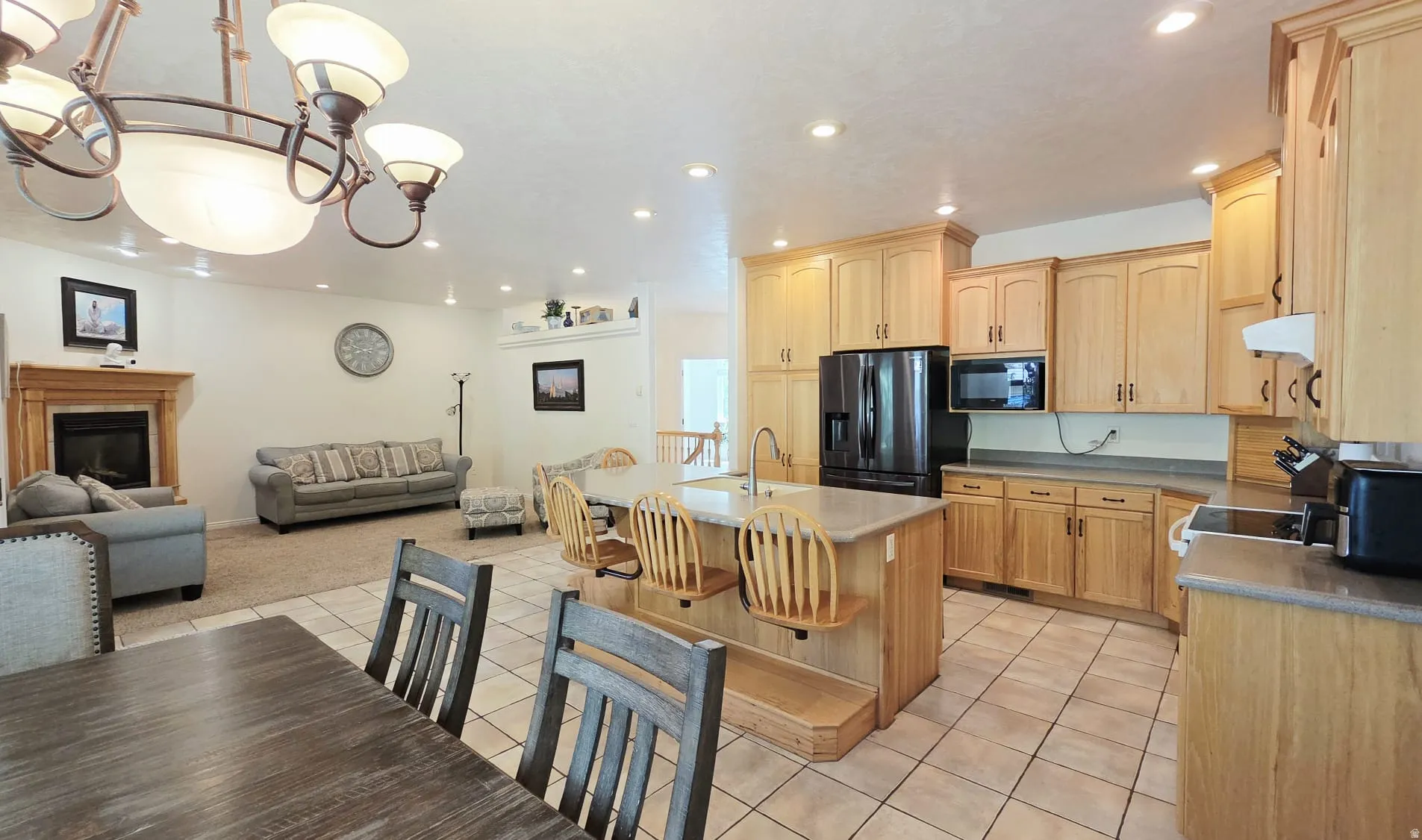 Open-concept living space featuring a kitchen with light wood cabinetry, a center island with bar seating, and tile flooring